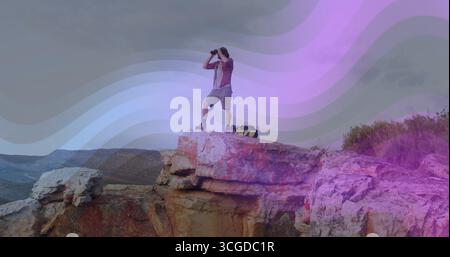 Einsamer Wanderer mit Stiefeln mit einem Fernglas scannen, während er auf Sandsteinklippe steht, mit Rucksack Stockfoto