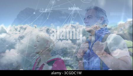 Ein stehendes Seniorenpaar blickt auf den Bergrücken in den Himmel und trägt Wanderrucksäcke mit digitaler Überlagerung Stockfoto