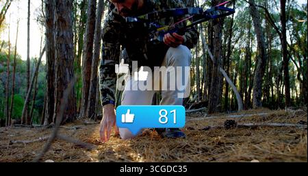 Kniender bärtiger Jäger, der die Spuren auf dem Boden des Kiefernwaldes inspiziert und den Verbundbogen unter Sonnenlicht hält Stockfoto