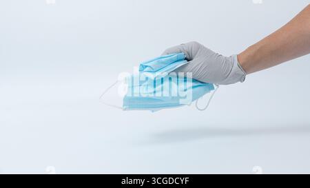 Die Hand, die einen medizinischen Handschuh trägt, hält eine Reihe gebrauchter blauer chirurgischer Masken, die Hygienepraktiken und Abfallwirtschaft im Gesundheitswesen zeigen Stockfoto