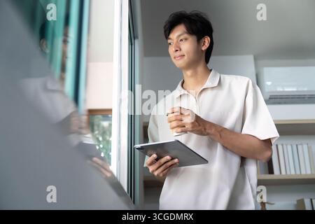 Morgenroutine. Junger Mann mit Tablet und Kaffee, genießen die Aussicht. Stockfoto