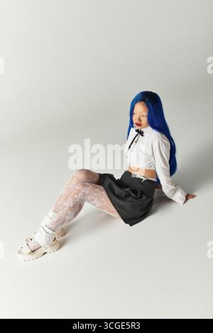 Stilvolle junge Frau sitzt anmutig und zeigt ihr einzigartiges blaues Haar und ihr modisches Ensemble. Stockfoto