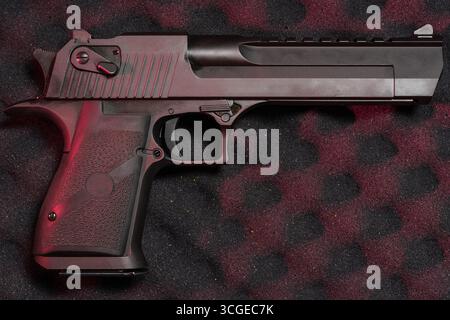 Eine halbautomatische Großkaliber-Pistole mit mattschwarzer Oberfläche, die unter dramatischer roter Beleuchtung auf einer strukturierten Oberfläche aufliegt. Stockfoto