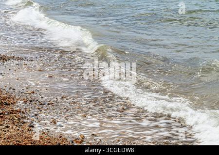 Verschwommene Wellen an der Küste des Kieselstrands in Whitstable an der Nordküste von Kent. Eine lange Belichtung führt zu einem verschwommenen Effekt. Stockfoto