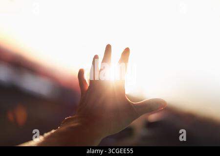 Ein starker, brillanter Lichtstrahl, der durch die Arme und Finger strahlt, streckte sich in Richtung der hellen Sonne aus. Stockfoto