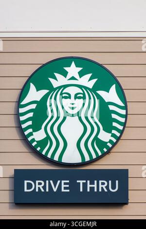 Starbucks-Logo und Drive-Thru-Schild auf einer hellbraunen holzgetäfelten Außenwand. Stockfoto