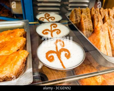 Baklava und cremiges Dessert mit Zimtdekoration in Glasvitrine einer traditionellen Bäckerei. Esskultur, süße Zubereitung, orientalisch Stockfoto