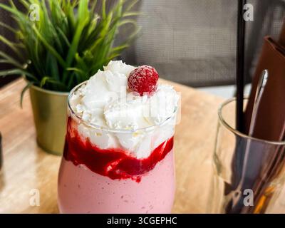 Erdbeermilkshake mit Schlagsahne und Himbeere serviert im Glas am Coffee-Tisch. Süßes Getränk, Dessert, Erfrischung, Lifestyle Stockfoto