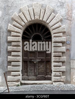 Alte Holzbogentür mit rustikalem Steinrahmen in einem historischen Gebäude in Latium, Italien. Architektonische Details. Stockfoto