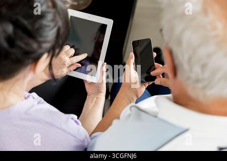 Ältere Männer und Frauen halten Smartphone und Tablet mit leeren Bildschirmen, perfekt für Kopierraum, Mockup-Design oder Platzierung digitaler Inhalte, Konzept o Stockfoto