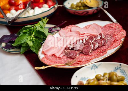 Eine wunderschön gestaltete italienische Wurstplatte bietet verschiedene Wurstwaren, frisches Basilikum und lebendiges Gemüse. Perfekt für Versammlungen und Gour Stockfoto