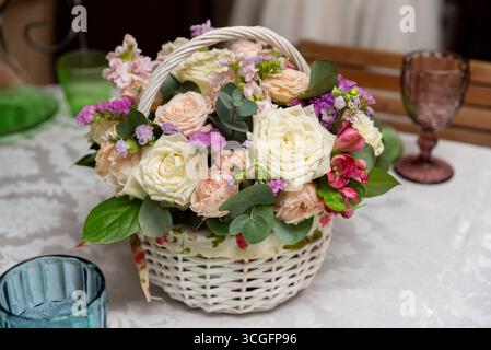 Ein wunderschöner Korb mit einer Vielzahl eleganter Blumen, darunter Rosen und Grün, perfekt als Herzstück zu besonderen Anlässen oder zum Zelt Stockfoto