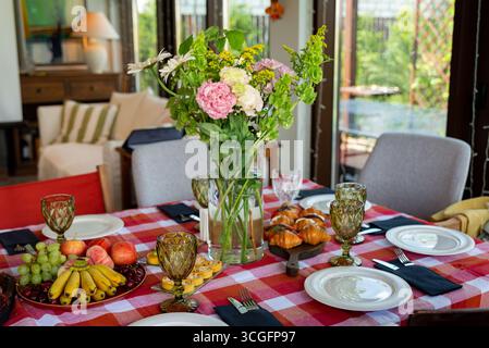 Ein wunderschön gedeckter Esstisch mit einem lebendigen Blumenpult, umgeben von elegantem Geschirr und einer Auswahl an frischem Obst und Gebäck. p Stockfoto