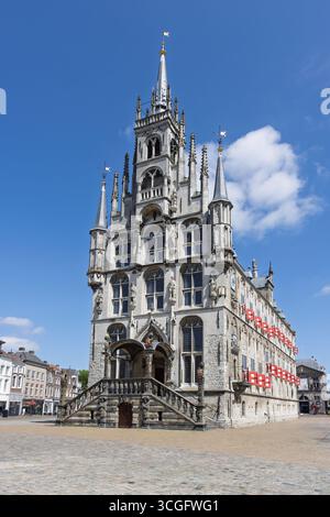 Das prächtige gotische Rathaus von Gouda steht prominent auf dem Marktplatz unter einem hellblauen Himmel mit ein paar Wolken. Stockfoto