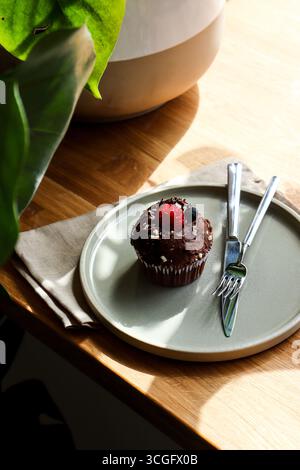 Ein köstlicher Vanille-Cupcake mit weißem Zuckerguss, einer Heidelbeere und einer Zitronenscheibe auf einer rustikalen Keramikplatte mit einem Löffel, mit einem zweiten Cupcake Stockfoto