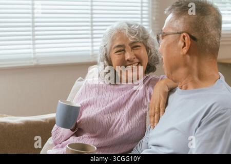 Glückliches Paar, das schöne Zeit zusammen in einem gemütlichen, modernen Zuhause verbringt. Sie unterhalten sich, trinken Kaffee, während die Frau auf einem Sofa sitzt und Stockfoto