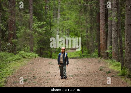Junge, der allein durch den Forest Path geht, umgeben von hohen Bäumen Stockfoto