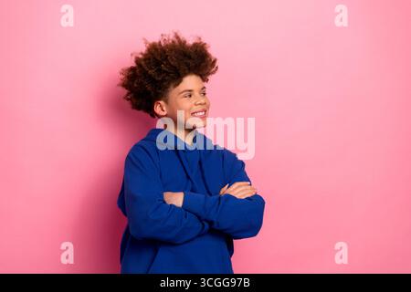 Fröhlicher Junge im lässigen blauen Hoodie mit überkreuzten Armen auf rosa Hintergrund, der Glück und stilvolle Jugendlichkeit darstellt Stockfoto