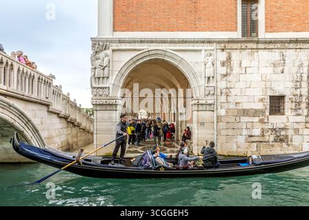 Venedig, Italien - 11. Februar 2025: Ein Gondoliere in traditioneller Kleidung fährt mit Touristen entlang eines Kanals in Venedig in der Nähe der Soupirs-Brücke Stockfoto