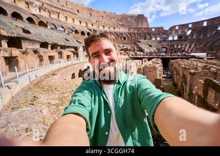 Fröhlicher Mann, der ein glückliches Selfie mit dem kolosseum im Hintergrund macht. Stockfoto