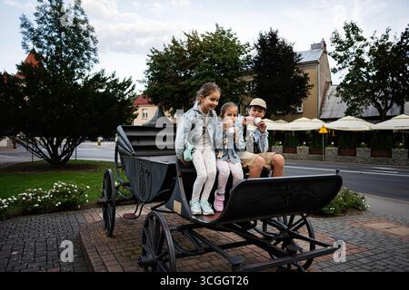 Drei Kinder sitzen in Lancut, Polen, auf einer alten Kutsche und genießen Eis. Stockfoto