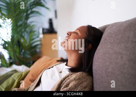 Eine junge Frau, die sich zu Hause auf einem Sofa entspannt. Stockfoto