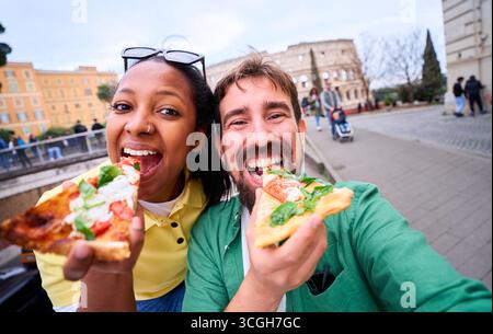 Glückliches Paar, das ein lustiges Selfie macht, während er Pizza vor dem kolosseum in Rom isst. Stockfoto