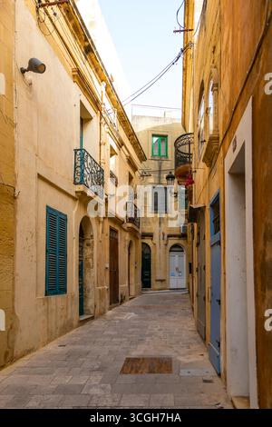 Gozo, Malta – 23. Juni 2021: Enge gepflasterte Gasse in Victoria mit traditioneller maltesischer Architektur, Holzläden und Balkonen mit Wro Stockfoto