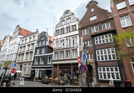Blick auf die Hamburger Speicherstadt mit historischen Klinker- und Backsteinbauten, Kopfsteinpflaster, Straßenschildern, Sitzgelegenheiten im Freien und bewölktem Himmel. Stockfoto