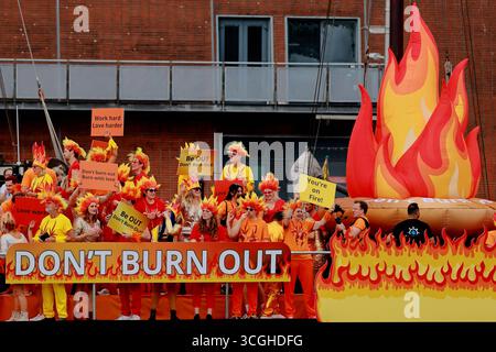 Aus nächster Nähe sehen Sie die Teilnehmer in orangefarbenen Kostümen mit Schildern auf einem Boot mit dem Titel „Don't Burn out“ an der Pride Amsterdam Canal Parade in Amsterdam, Niederlande. Stockfoto