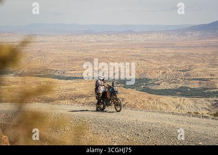 Fahrer auf Yamaha Tenere 700 Abenteuer-Motorrad in marokkanischen Wüstenbergen, Enduro-Tourenrad mit Gepäck auf Schotterpiste, weite trockene Landschaft Stockfoto