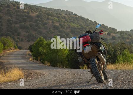 Yamaha Tenere 700 Abenteuer Motorrad auf einer Schotterstraße in den marokkanischen Bergen, Offroad-Tourenrad umgeben von malerischen Hügeln und Sonnenuntergang Stockfoto
