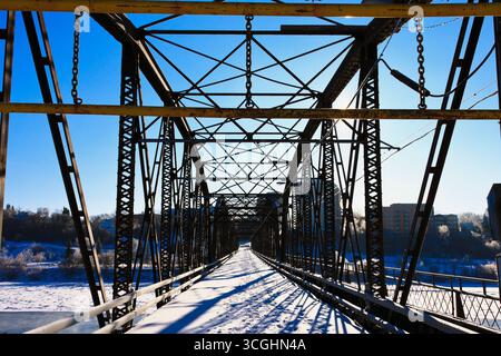 Schnee bedeckt die Flussufer, während sich die Traffic Bridge von Saskatoon über den gefrorenen South Saskatchewan River in einer malerischen Winterszene erstreckt. Stockfoto