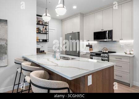 Küche mit Marmorarbeitsfläche und weißen Schränken. Die Arbeitsplatte ist von Stühlen und einem Waschbecken umgeben Stockfoto