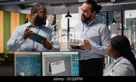 Ingenieure im Büro Brainstorming für Upgrades für innovative solarbetriebene Geräte. Teamwork-RD-Spezialisten, die tragbare Solarmodule ausprobieren und gemeinsam an der Verbesserung der Effizienz arbeiten, Kamera B Stockfoto