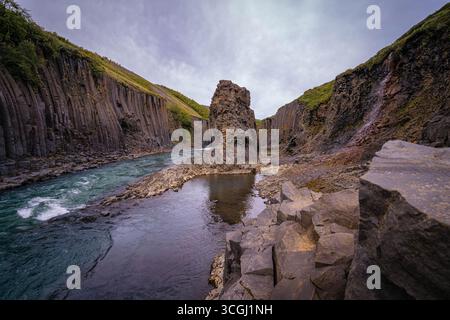 Der Stuðlagil Canyon in Ost-Island zeigt dramatische Basaltsäulen und einen türkisfarbenen Gletscherfluss, der sich durch steile vulkanische Wände und felsige Klippen schlängelt Stockfoto
