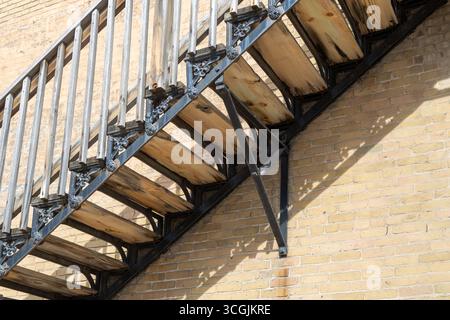 Vollformatansicht einer antiken Treppe aus Eisen und Holz, die an der Außenseite einer beigefarbenen Ziegelmauer aus dem 19. Jahrhundert angebracht ist, bei hellem Sonnenlicht Stockfoto