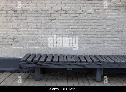 Voller Rahmen abstrakte Textur Hintergrund einer bläulich grauen Holzbank entlang einer grungy weiß gemalten Ziegelwand, die Verschleiß und abblätternde Farbe zeigt Stockfoto