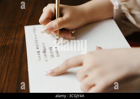 Frau, die chinesische Kalligraphie mit Goldstift auf Weißbuch schreibt Stockfoto