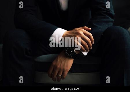 Mann im dunklen Anzug mit schwarzer Uhr und Hochzeitsband, Handdetails Stockfoto