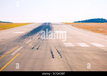 Landebahn mit zahlreichen Reifenrutschspuren, die häufige Landungen und Starts anzeigen. Die Start- und Landebahn ist von grasbewachsenen Flächen und Hügeln im Hintergrund umgeben Stockfoto