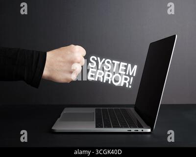 Faustschlag auf einen Laptop mit Systemfehlermeldungen auf dem Bildschirm, die Frustration und Wut über Computerprobleme zum Ausdruck bringen Stockfoto