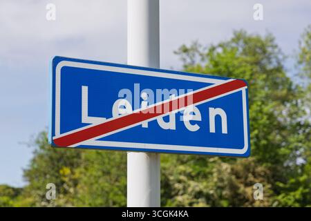 Ein Schild zum Ausgang der Stadt Leiden, mit einem diagonalen roten Balken, der das Verlassen der Stadtgrenze anzeigt, vor einem Hintergrund von grünen Bäumen und einem hellen Himmel. Stockfoto