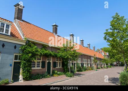Historisches Hofje in Delft, Niederlande, eine malerische Reihe traditioneller niederländischer Almshouses mit bezaubernden Fassaden und einer ruhigen, von Bäumen gesäumten Straße. Stockfoto