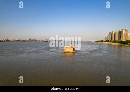 Ein historisches Gebäude befindet sich im ruhigen Fluss Yangtze, umgeben von der sich entwickelnden Stadtlandschaft der Stadt Ezhou, Provinz Hubei, China. Stockfoto
