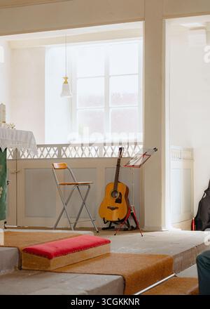 Sonnendurchfluteter Raum mit Akustikgitarre auf einem Ständer neben einem Klappstuhl und Notenständer. Die Lage bietet eine friedliche Atmosphäre, ideal Stockfoto