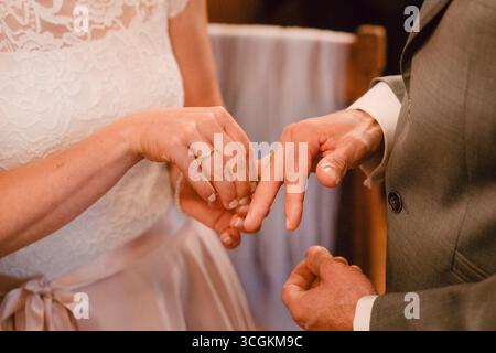 Nahaufnahme einer Braut, die während einer Hochzeitszeremonie einen Ring auf den Finger des Bräutigams legt. Das Bild fängt diesen bedeutenden Austausch mit Eleganz und ein Stockfoto