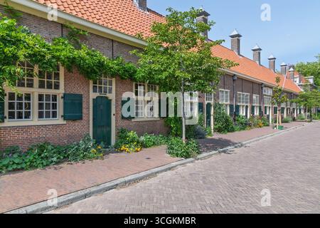 Charmante Reihe historischer Hofje-Gebäude in Delft, Niederlande, mit traditioneller niederländischer Architektur mit grünen Türen, Rollläden und üppigem Grün Stockfoto