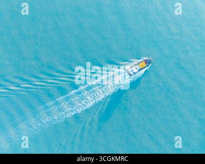 Ein kleines Schiff bewegt sich über ruhige Meeresgewässer und hinterlässt eine weiße Spur. Diese friedliche maritime Szene befindet sich in der Nähe von Xiamen, China. Stockfoto