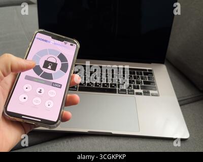 Man steuert Smart-Home-Geräte mithilfe der App für das Mobiltelefon auf dem Hintergrund des Arbeitstisches eines Geschäftsmannes im Innenraum des Home-Office. Konzept von Stockfoto